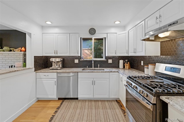 kitchen with appliances with stainless steel finishes, tasteful backsplash, white cabinetry, sink, and light stone countertops