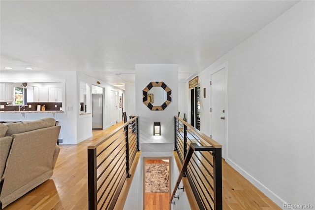 hallway with baseboards, a sink, light wood finished floors, and an upstairs landing