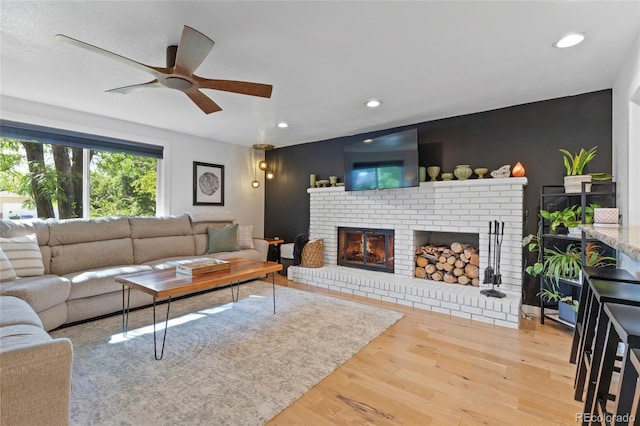 living room with a brick fireplace, a ceiling fan, wood finished floors, and recessed lighting