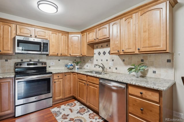 kitchen featuring appliances with stainless steel finishes, a sink, wood finished floors, light stone countertops, and backsplash
