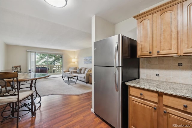 kitchen with freestanding refrigerator, decorative backsplash, dark wood-style flooring, light stone counters, and open floor plan