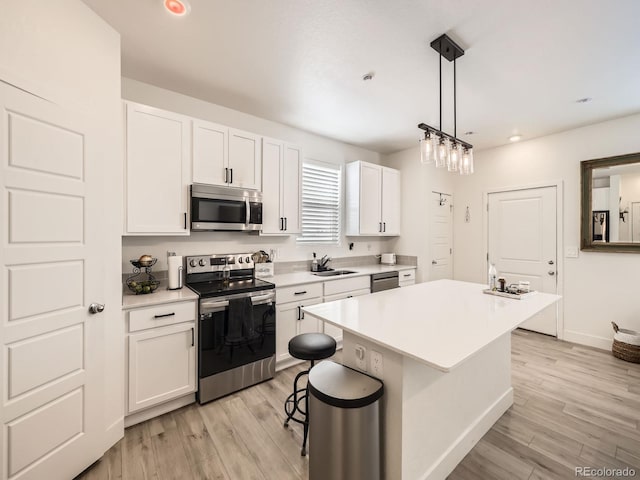 kitchen with hanging light fixtures, white cabinetry, a center island, light hardwood / wood-style floors, and stainless steel appliances