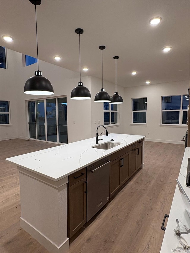 kitchen featuring pendant lighting, sink, a large island, light stone counters, and dark brown cabinetry