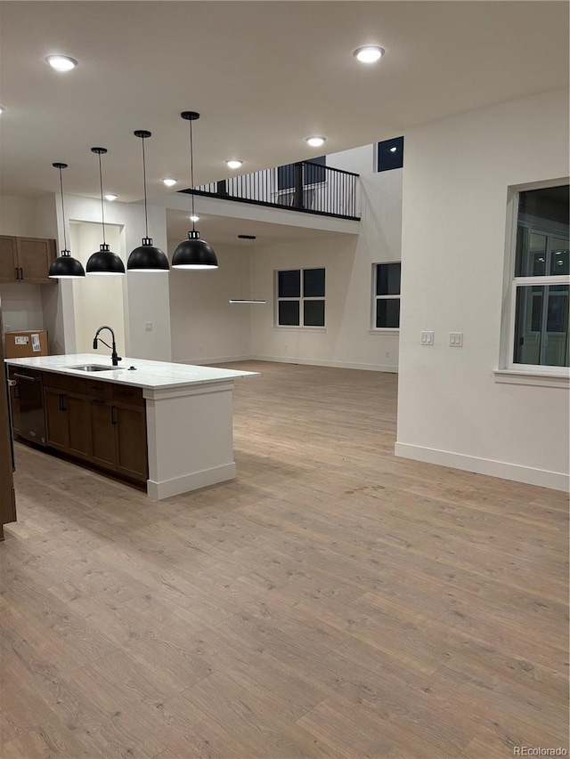 kitchen with decorative light fixtures, light hardwood / wood-style flooring, a kitchen island with sink, and sink