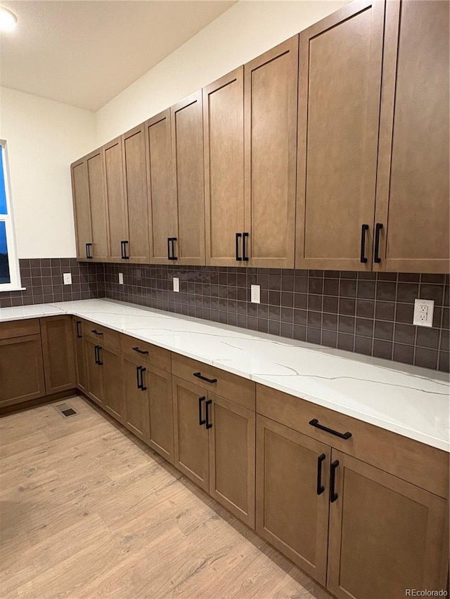 kitchen with decorative backsplash, light stone countertops, and light hardwood / wood-style flooring