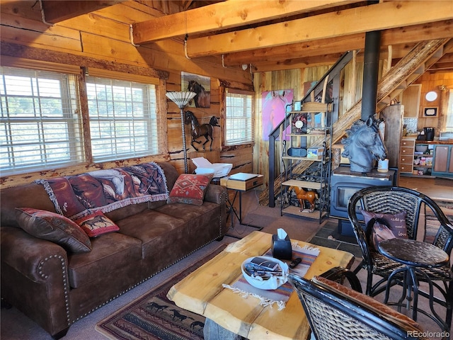 living room featuring beamed ceiling, a wood stove, and wooden walls