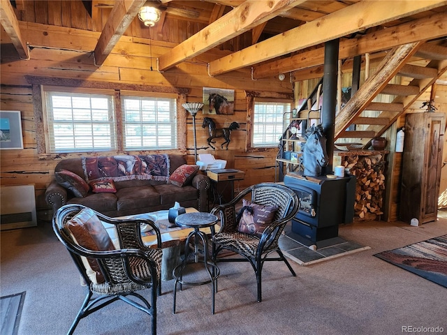 carpeted living room with beamed ceiling, a healthy amount of sunlight, a wood stove, and wooden walls