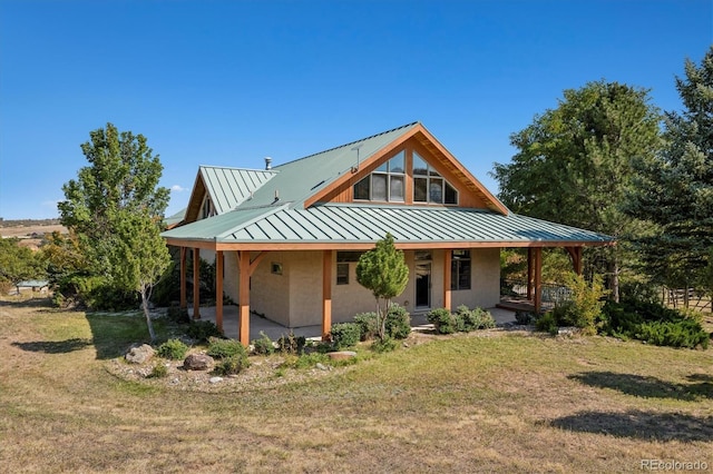 rear view of property with stucco siding, metal roof, a porch, a yard, and a standing seam roof