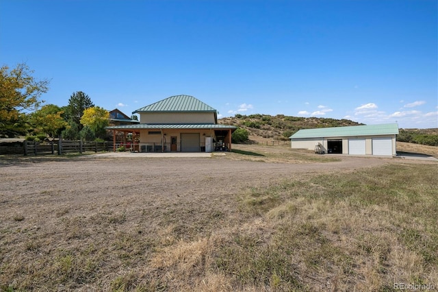 rear view of house with metal roof, an outdoor structure, fence, and a detached garage