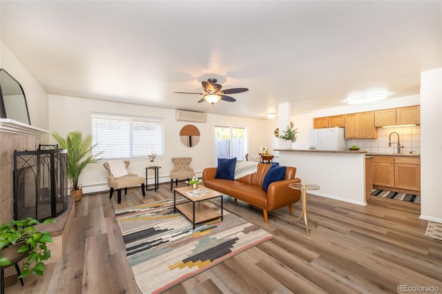 living room with hardwood / wood-style floors, a wall mounted air conditioner, a tile fireplace, sink, and ceiling fan