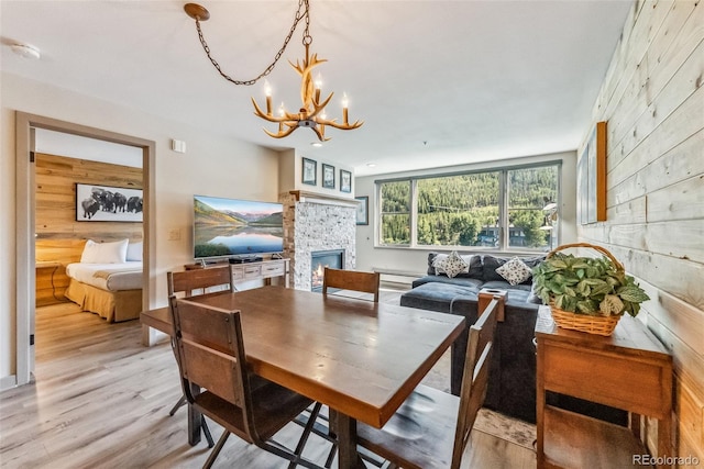 dining space with light hardwood / wood-style floors, a fireplace, wood walls, and an inviting chandelier