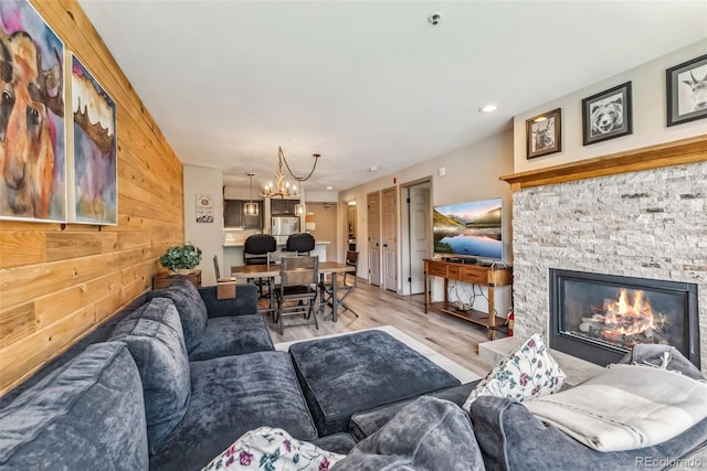 living room with an inviting chandelier, light wood-type flooring, a fireplace, and wooden walls