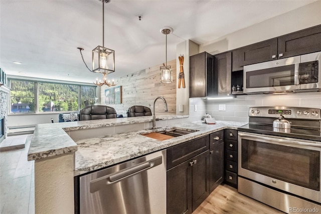 kitchen with pendant lighting, light wood-type flooring, sink, a notable chandelier, and stainless steel appliances