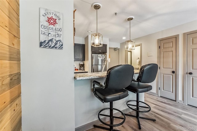 kitchen with pendant lighting, light stone counters, a breakfast bar area, kitchen peninsula, and light hardwood / wood-style flooring