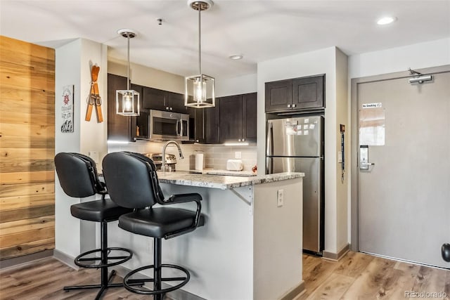 kitchen featuring dark brown cabinets, backsplash, appliances with stainless steel finishes, a kitchen breakfast bar, and light hardwood / wood-style floors