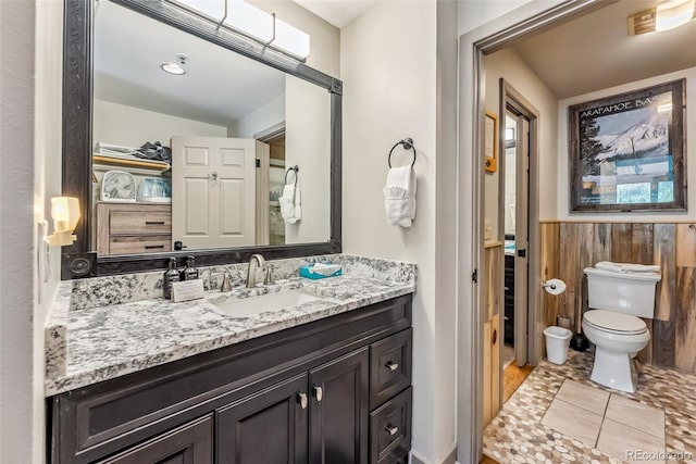 bathroom with wood walls, vanity, toilet, and tile patterned floors