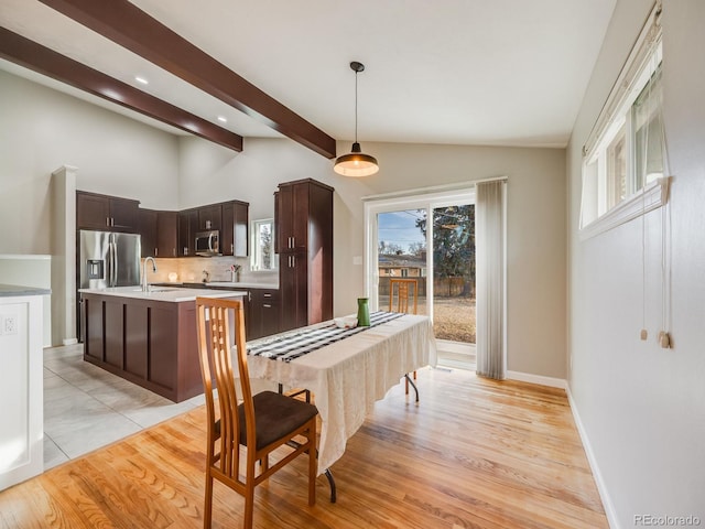 dining area featuring sink, lofted ceiling with beams, and light wood-type flooring