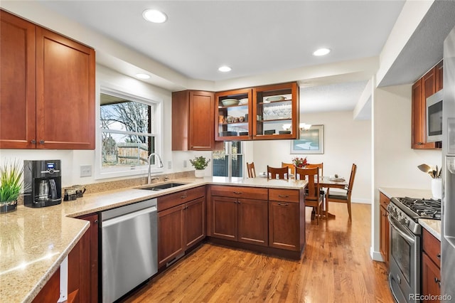 kitchen with stainless steel appliances, recessed lighting, a sink, light stone countertops, and light wood-type flooring