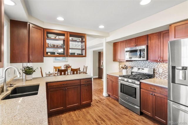 kitchen featuring light wood finished floors, appliances with stainless steel finishes, light stone counters, and a sink