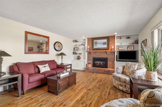 living room with a textured ceiling, light wood finished floors, a brick fireplace, and built in shelves