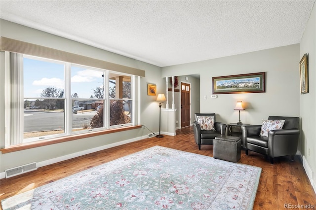 living area featuring dark wood-style floors, visible vents, a textured ceiling, and baseboards