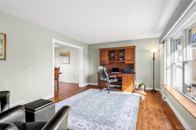 office area featuring a textured ceiling, light wood finished floors, visible vents, and baseboards