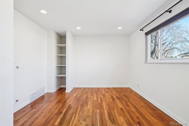 unfurnished room featuring built in shelves and wood-type flooring