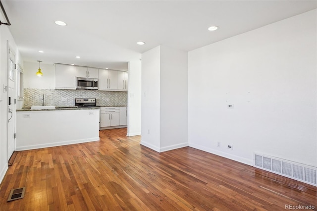 kitchen with hardwood / wood-style floors, white cabinets, decorative backsplash, appliances with stainless steel finishes, and decorative light fixtures