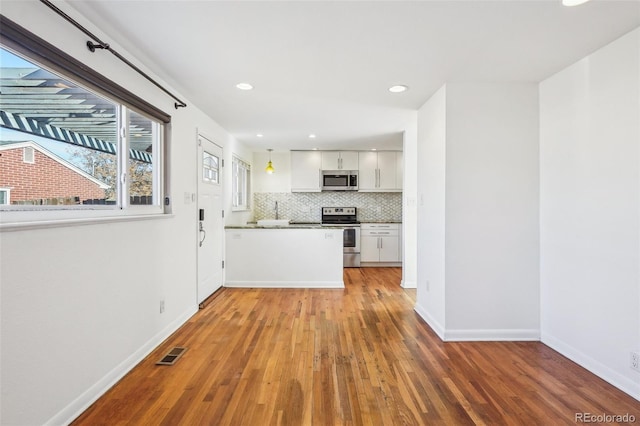 kitchen with pendant lighting, backsplash, white cabinets, appliances with stainless steel finishes, and wood-type flooring