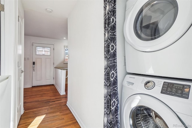 clothes washing area with hardwood / wood-style flooring and stacked washer / drying machine