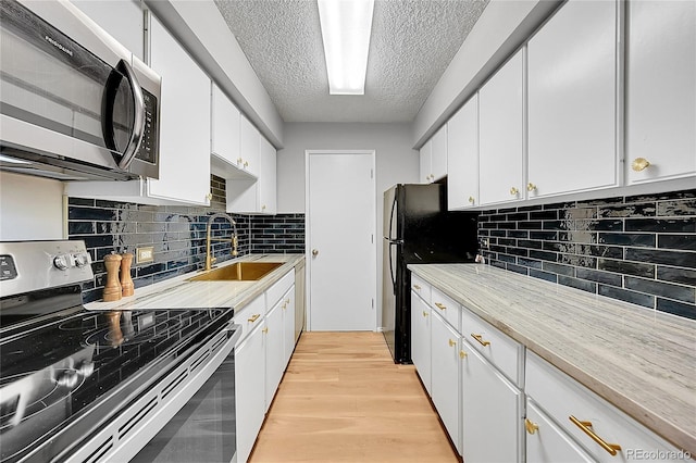 kitchen featuring sink, a textured ceiling, light wood-type flooring, stainless steel appliances, and white cabinets