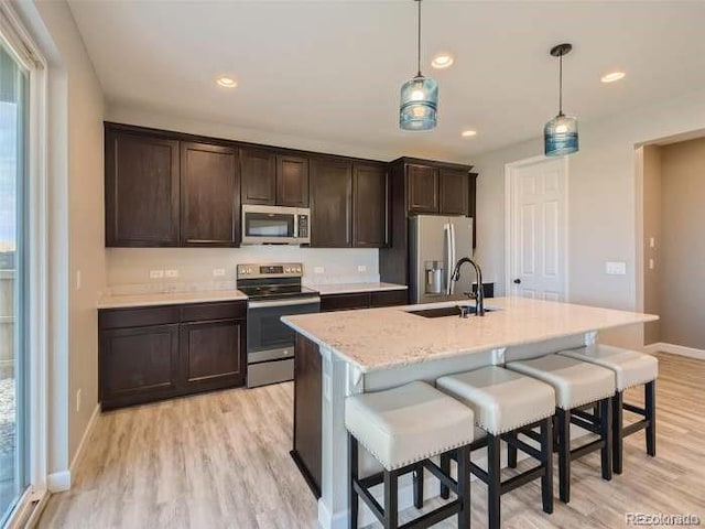 kitchen with light hardwood / wood-style flooring, stainless steel appliances, sink, dark brown cabinets, and decorative light fixtures