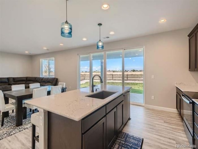 kitchen featuring light hardwood / wood-style flooring, dark brown cabinets, light stone counters, decorative light fixtures, and sink