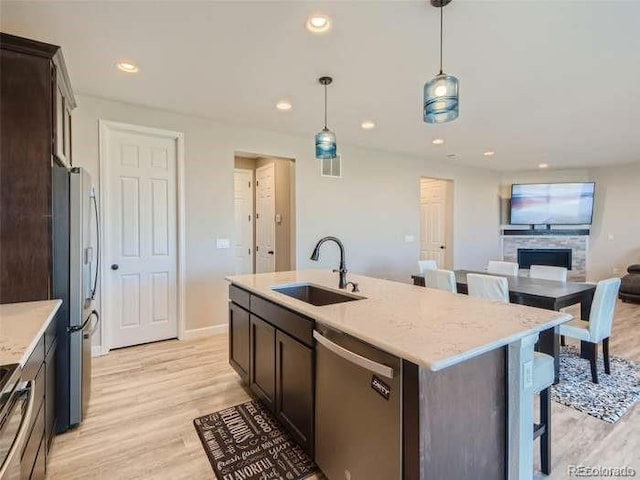 kitchen featuring appliances with stainless steel finishes, sink, pendant lighting, a kitchen island with sink, and light wood-type flooring