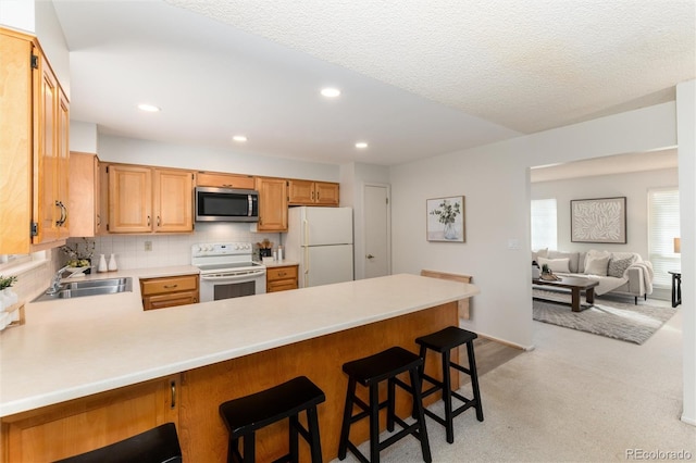 kitchen featuring white appliances, a kitchen breakfast bar, kitchen peninsula, sink, and backsplash