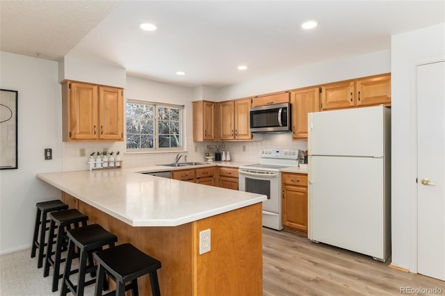 kitchen with sink, white appliances, light wood-type flooring, kitchen peninsula, and backsplash