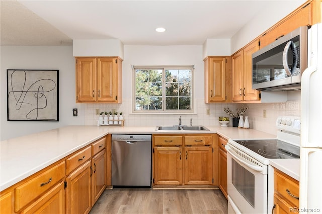 kitchen with appliances with stainless steel finishes, light wood-type flooring, backsplash, and sink