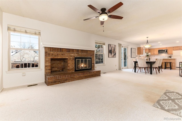 carpeted living room featuring a brick fireplace, a textured ceiling, and ceiling fan