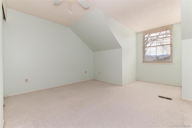 additional living space with a textured ceiling, light colored carpet, vaulted ceiling, and ceiling fan