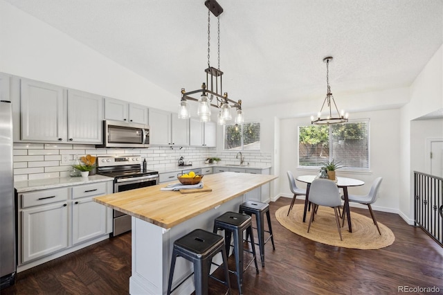 kitchen with decorative backsplash, a kitchen bar, appliances with stainless steel finishes, a sink, and butcher block countertops