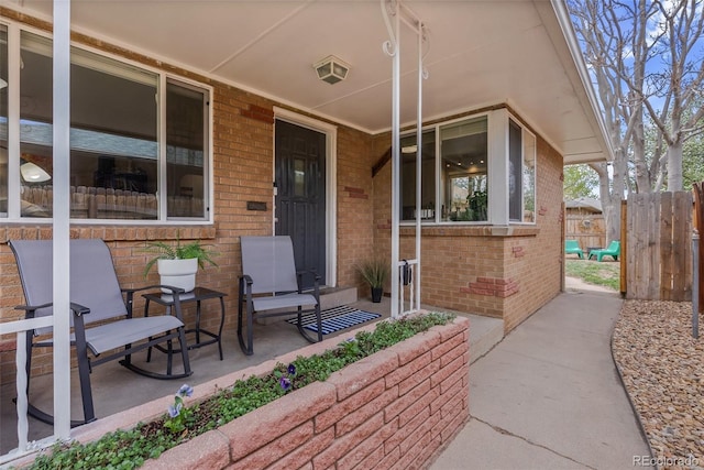 entrance to property featuring fence, a porch, and brick siding