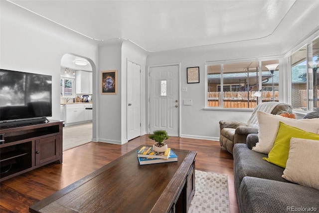 living room featuring arched walkways, baseboards, and wood finished floors
