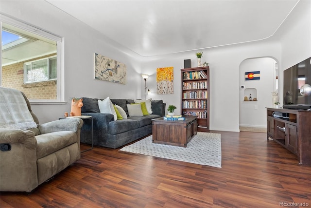 living room featuring arched walkways, baseboards, and dark wood-style flooring