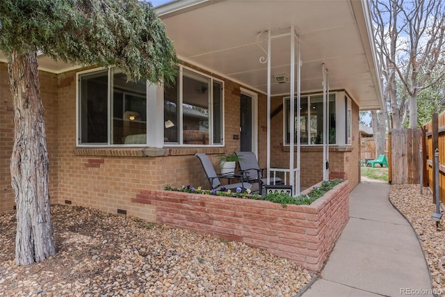 view of front of home with fence, covered porch, brick siding, and crawl space