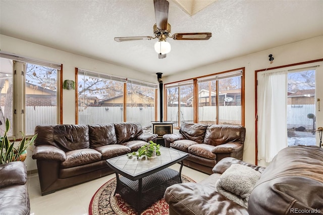 living room featuring a wood stove, ceiling fan, light tile patterned floors, and a textured ceiling