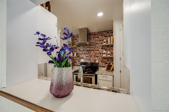 bar with stainless steel range with electric stovetop, wall chimney exhaust hood, brick wall, sink, and white cabinets