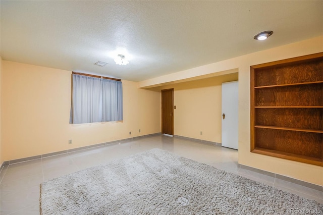 empty room featuring built in features, light tile patterned flooring, and a textured ceiling