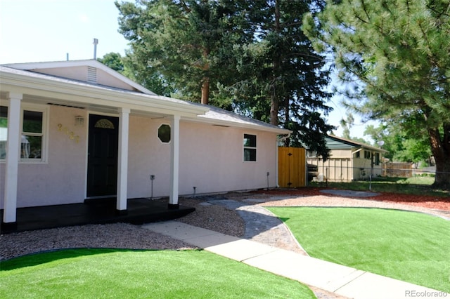 exterior space with stucco siding, covered porch, a front lawn, and fence