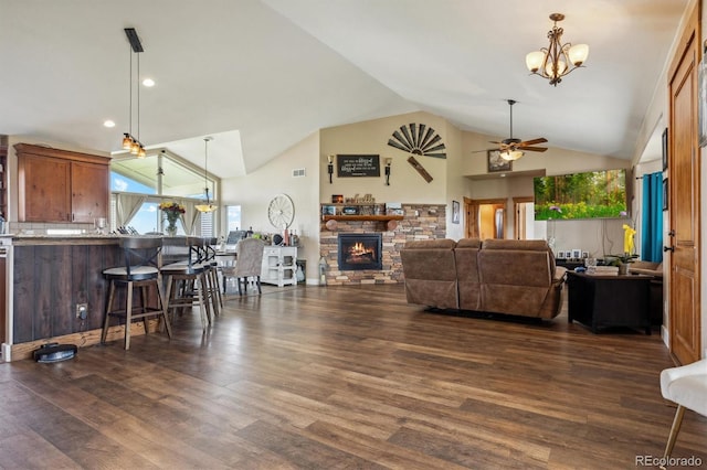 living room featuring ceiling fan with notable chandelier, high vaulted ceiling, dark wood-type flooring, and a stone fireplace