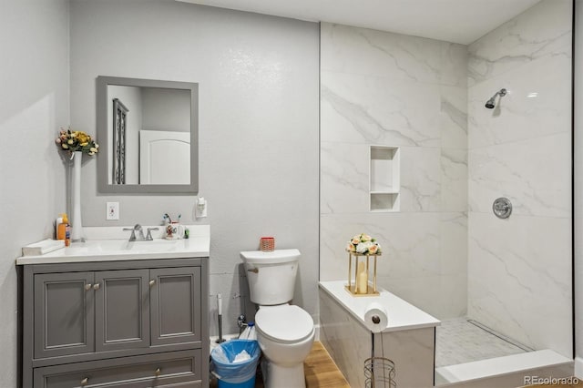 bathroom with a tile shower, hardwood / wood-style floors, vanity, and toilet